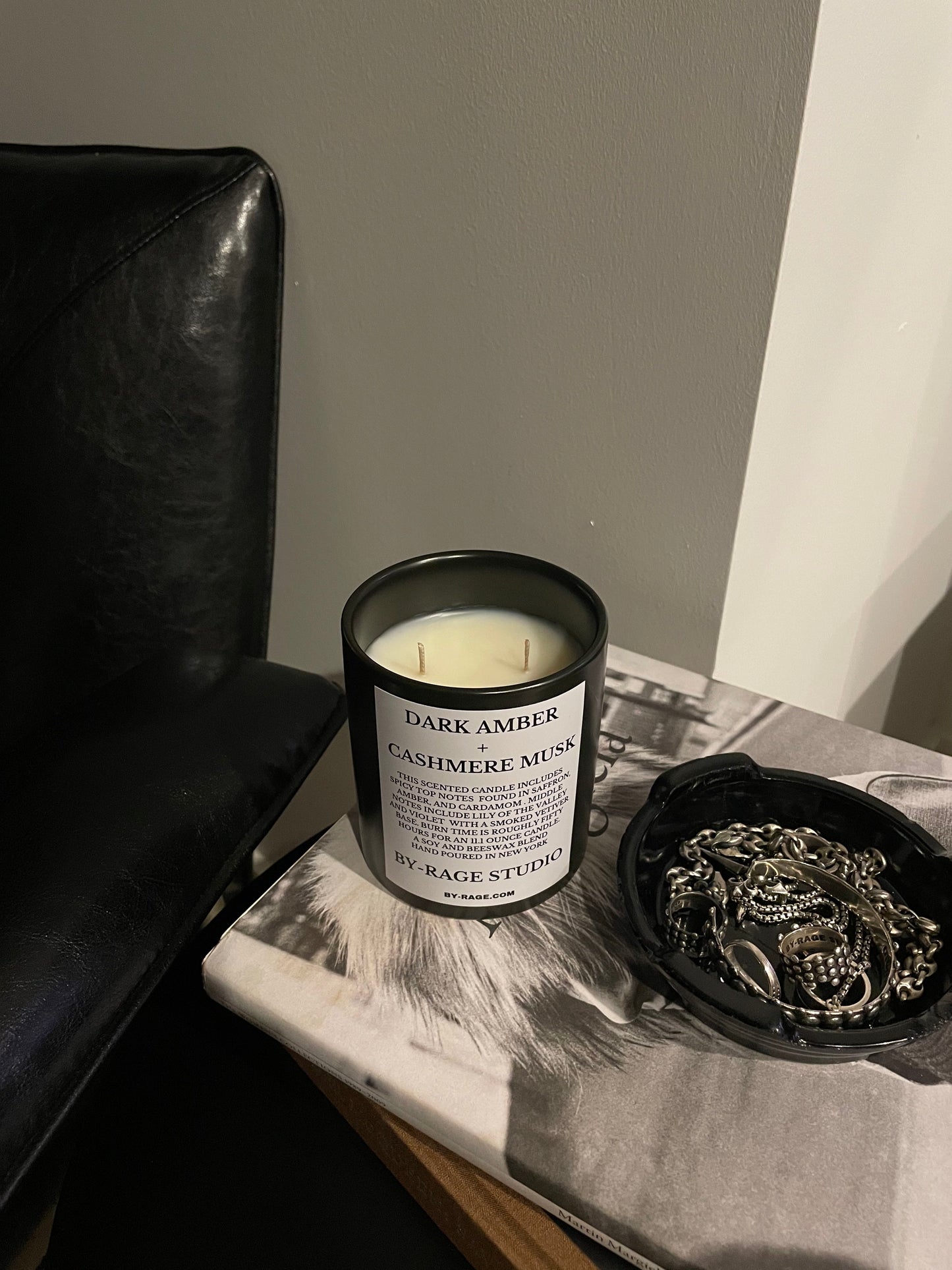 Modern scented candle in minimal living room and side table aesthetic . Maison Martin Margiela coffee table book with jewelry holder or black ashtray.