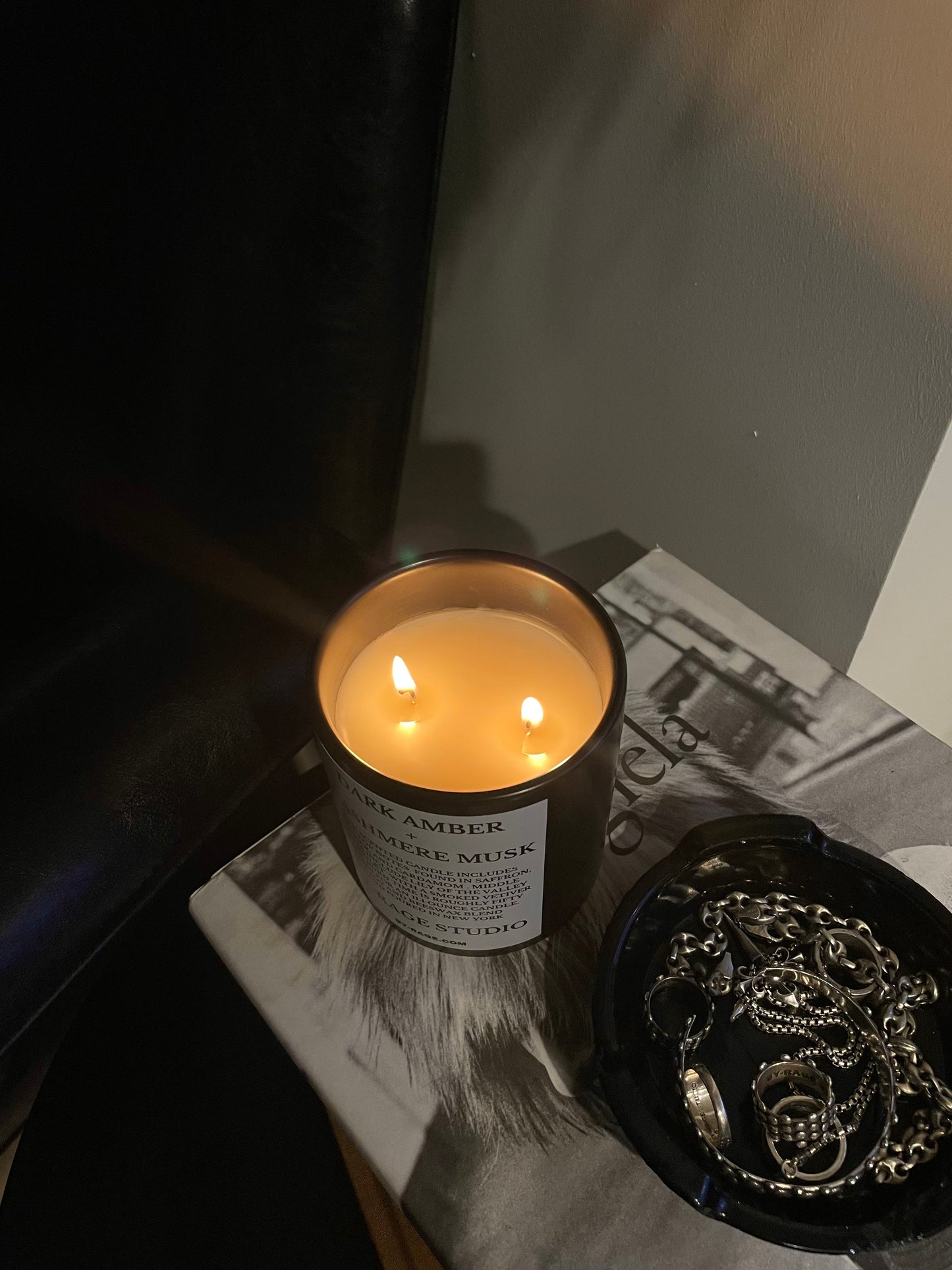 Modern scented candle in minimal living room and side table aesthetic . Maison Martin Margiela coffee table book with jewelry holder or black ashtray.